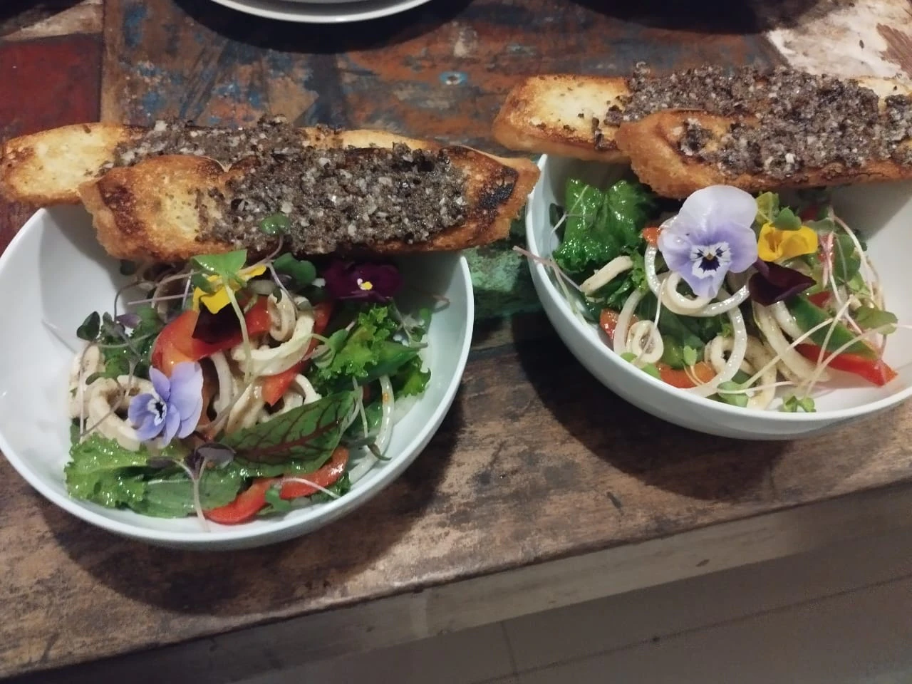 Two bowls of calamari salad topped with edible flowers and grilled bread