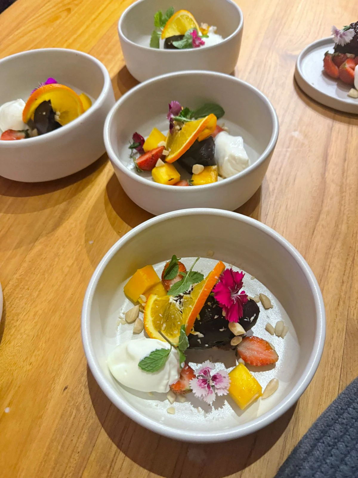 Dessert bowls of chocolate, mango, strawberry and cream with edible flowers