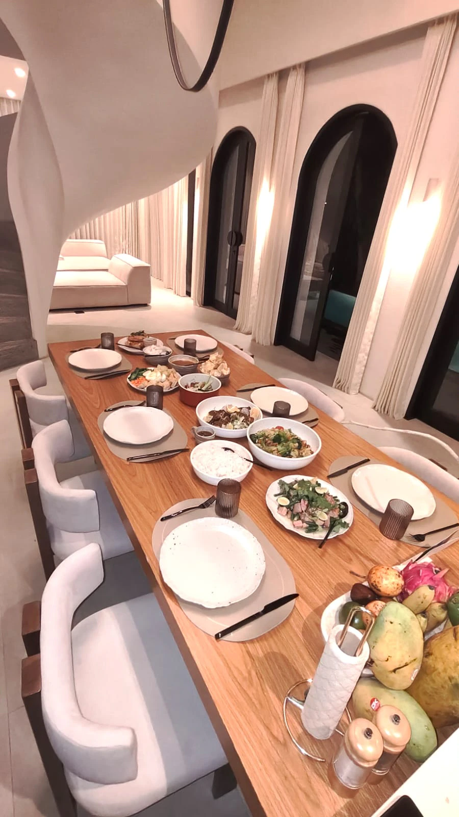 A long dining table set for dinner inside a Bali villa, lit by warm lamps